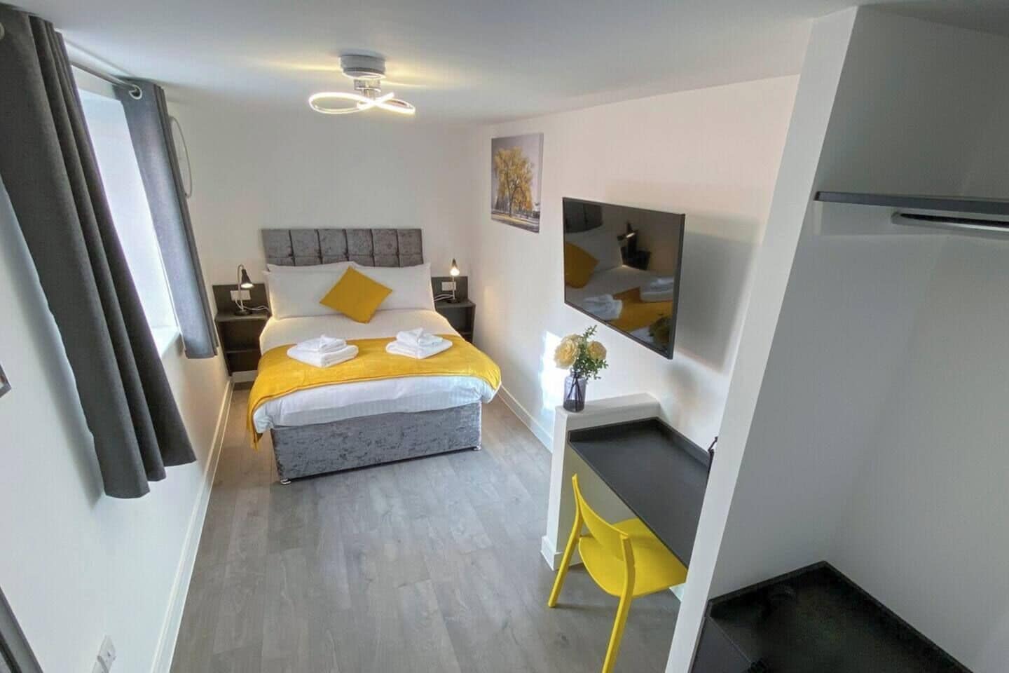 Una habitación de hotel moderna con cama, mesita de noche, silla y un pequeño escritorio.