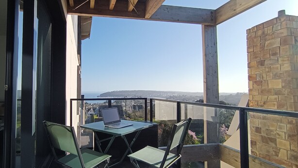 A balcony with a laptop on a table, two chairs, and a view of a cityscape. - Cocon à Crozon - Superb new apartment with view (Crozon)