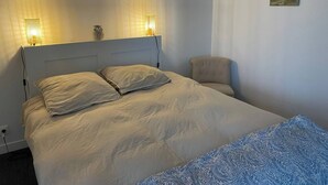A bedroom with a bed, two bedside lamps, a chair, and a small painting on the wall. - Cocon à Crozon - Superb new apartment with view (Crozon)