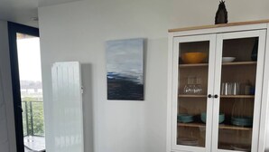 A modern dining area with a round table, white chairs, a cabinet with glass doors, and a painting on the wall. - Cocon à Crozon - Superb new apartment with view (Crozon)