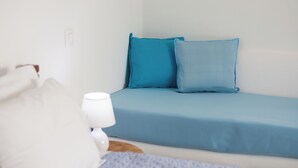 A bed with a white pillow and a blue mattress, a white bedside lamp, and a wooden nightstand. -  Deluxe apartment with panoramic sea view located on the hill of Provatas (Milos)