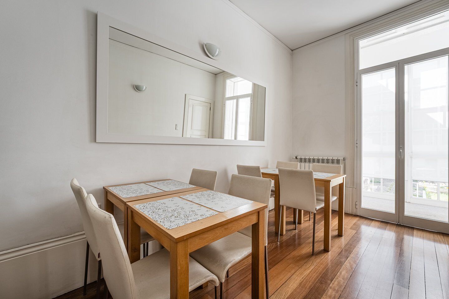 A dining area with a wooden table and chairs, a large mirror on the wall, and a sliding glass door leading to a balcony.