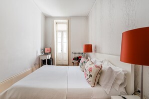 Habitación de hotel con una cama grande, un escritorio con computadora, una silla y ventana con vista al exterior.