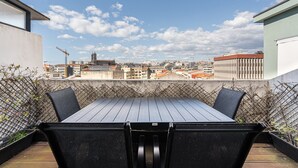 Una terraza en la azotea con mesa y sillas, vistas panorámicas de la ciudad y cielo despejado.
