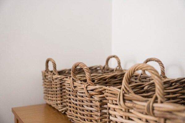 Three wicker baskets with handles on a wooden table against a plain wall.