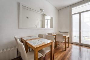 Uma área de refeições com mesa e cadeiras de madeira, um espelho grande na parede e uma porta de vidro deslizante que dá para uma varanda.