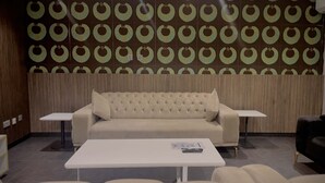 Un espace de détente moderne avec un canapé capitonné, une table blanche et un mur orné d’un motif.