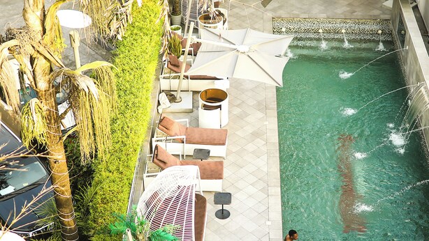 Une piscine extérieure dotée de chaises longues et de parasols, entourée de verdure et bordée d’une terrasse carrelée.