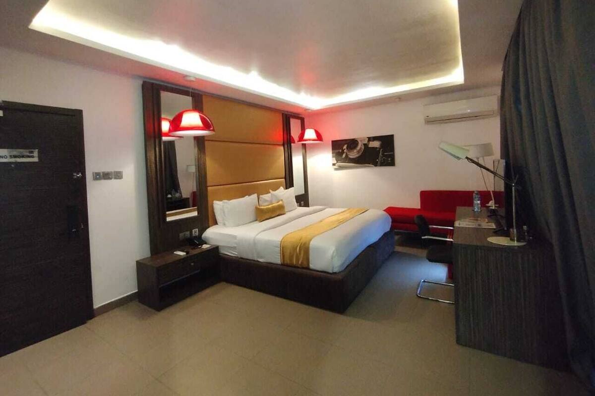 Una habitación de hotel moderna con una cama grande, mesitas de noche, un escritorio y un sofá rojo.