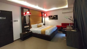 Une chambre d’hôtel moderne avec un grand lit, des tables de chevet, un bureau et un canapé rouge.