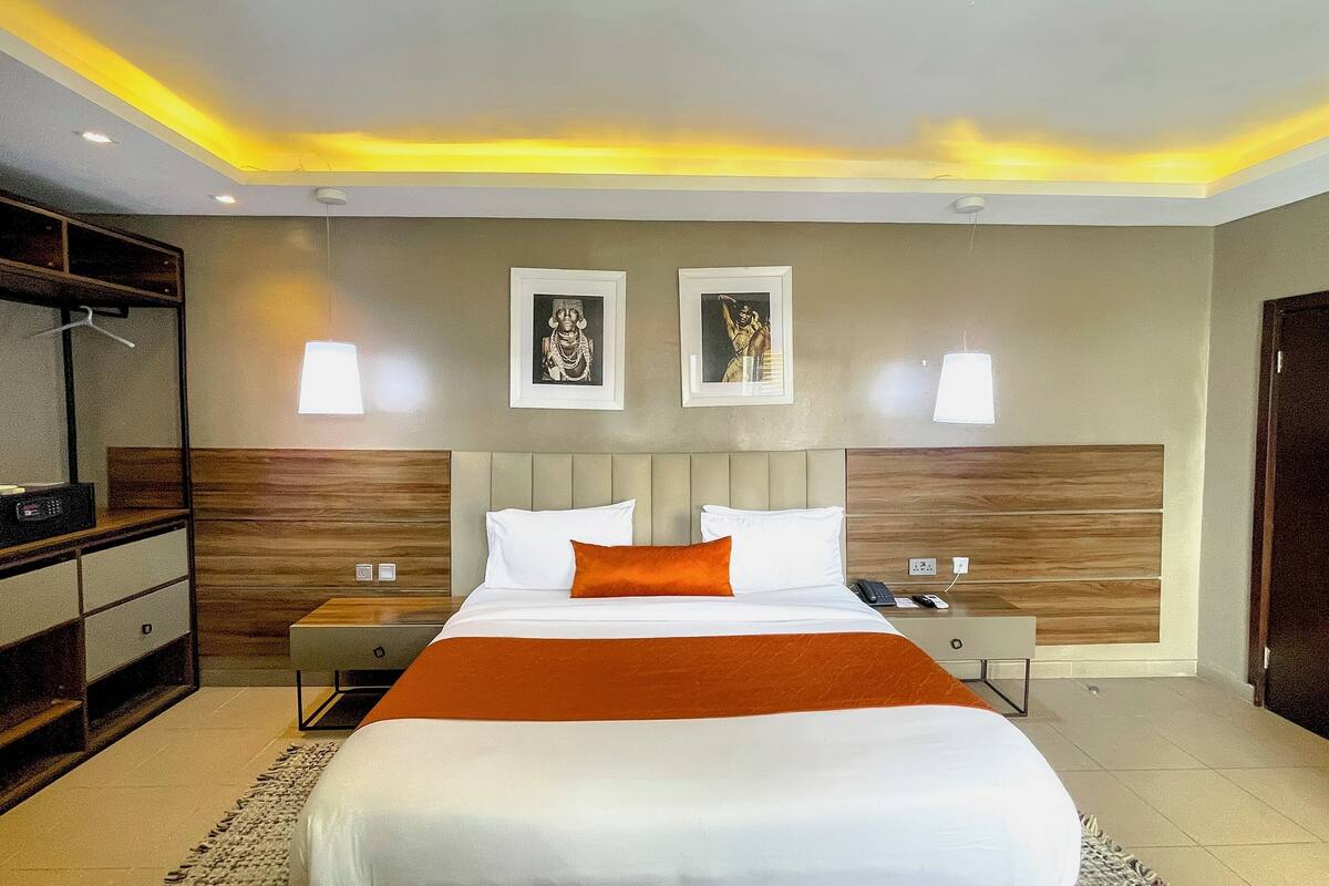 Habitación de hotel con una cama grande, dos mesitas de noche, un armario y un televisor sobre un mueble.