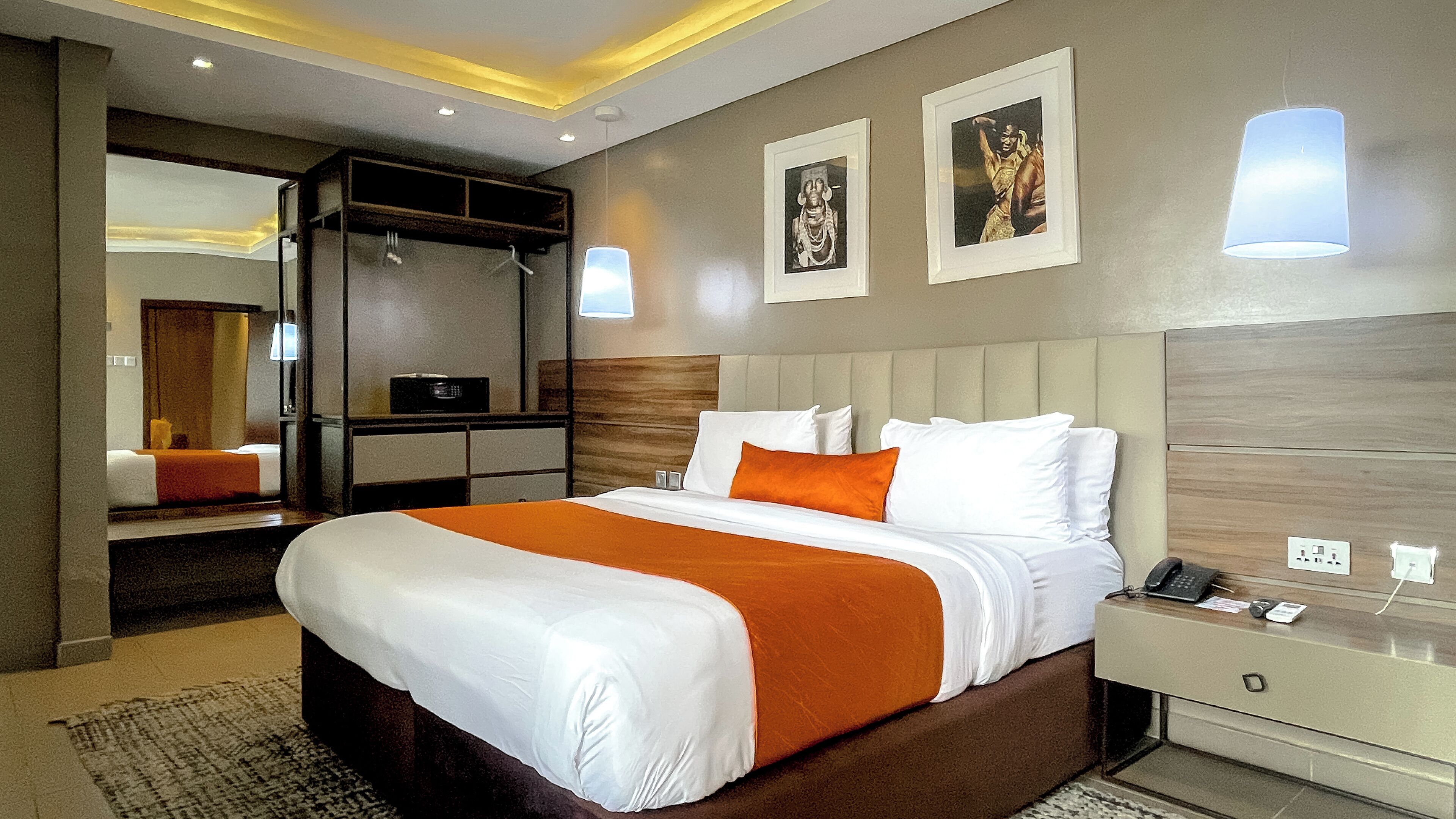 Een hotelkamer met een groot bed, een nachtkastje met telefoon, een spiegel en een kledingkast.