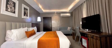 Habitación de hotel con una cama grande, un escritorio con computadora, televisión y minibar.