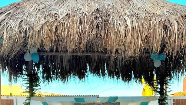 Una piscina con techo de paja, rodeada de sillones blancos y un pequeño bar.