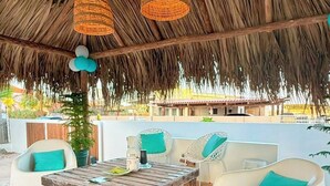 Un espacio al aire libre con techo de paja, cubierta de madera y mobiliario de mimbre.