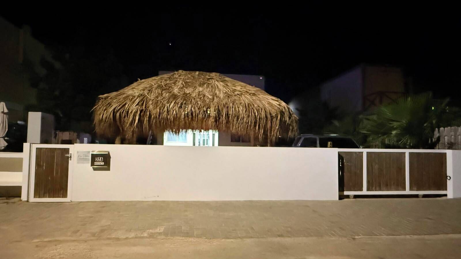 A thatched-roof structure with a white wall and a gated entrance.