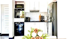 Una cocina moderna con armarios blancos, un refrigerador de acero inoxidable y una cafetera en la encimera.