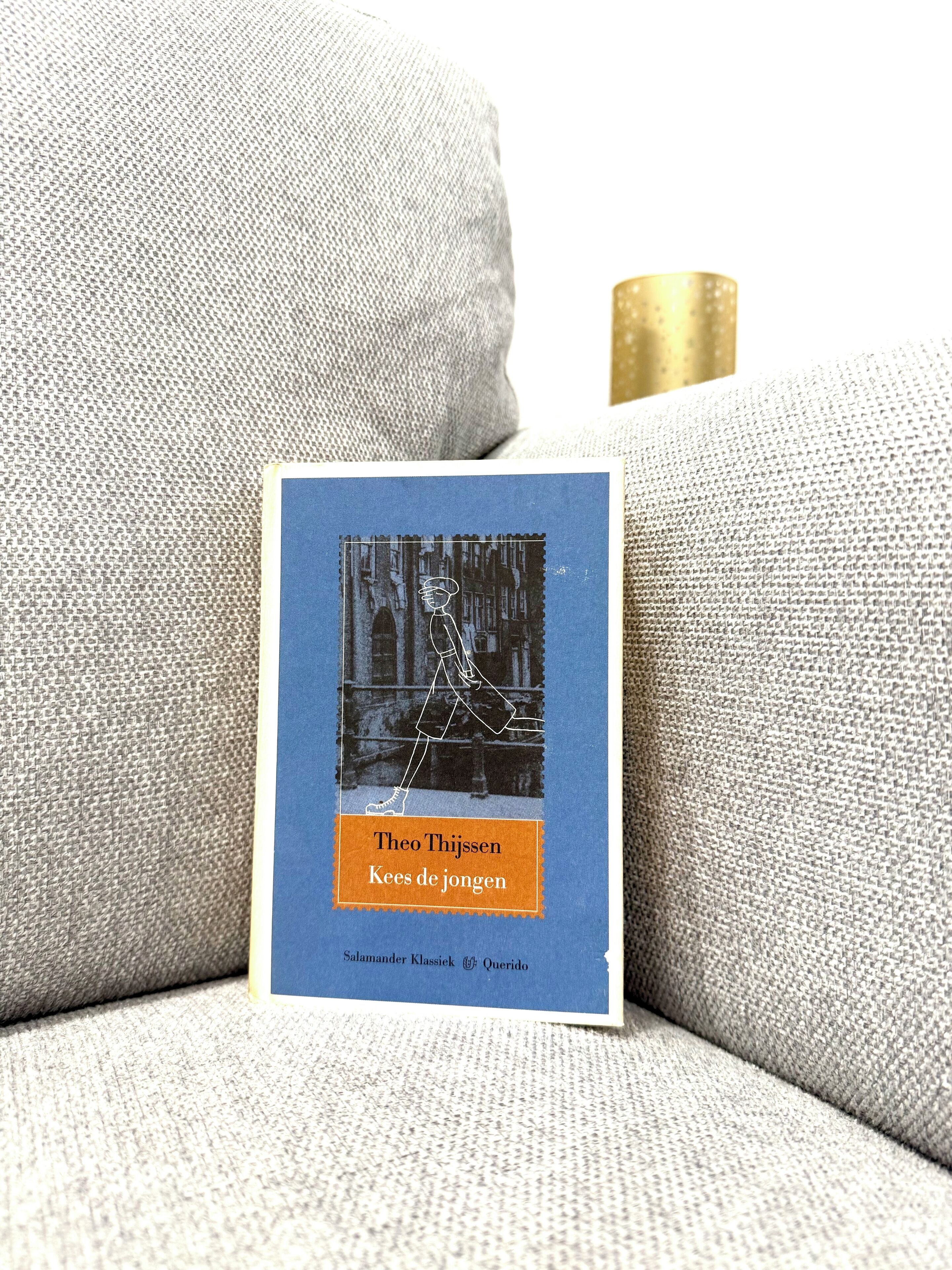 Un livre intitulé « Kees de jongen » de Theo Thijssen, posé sur un canapé gris à la texture particulière.
