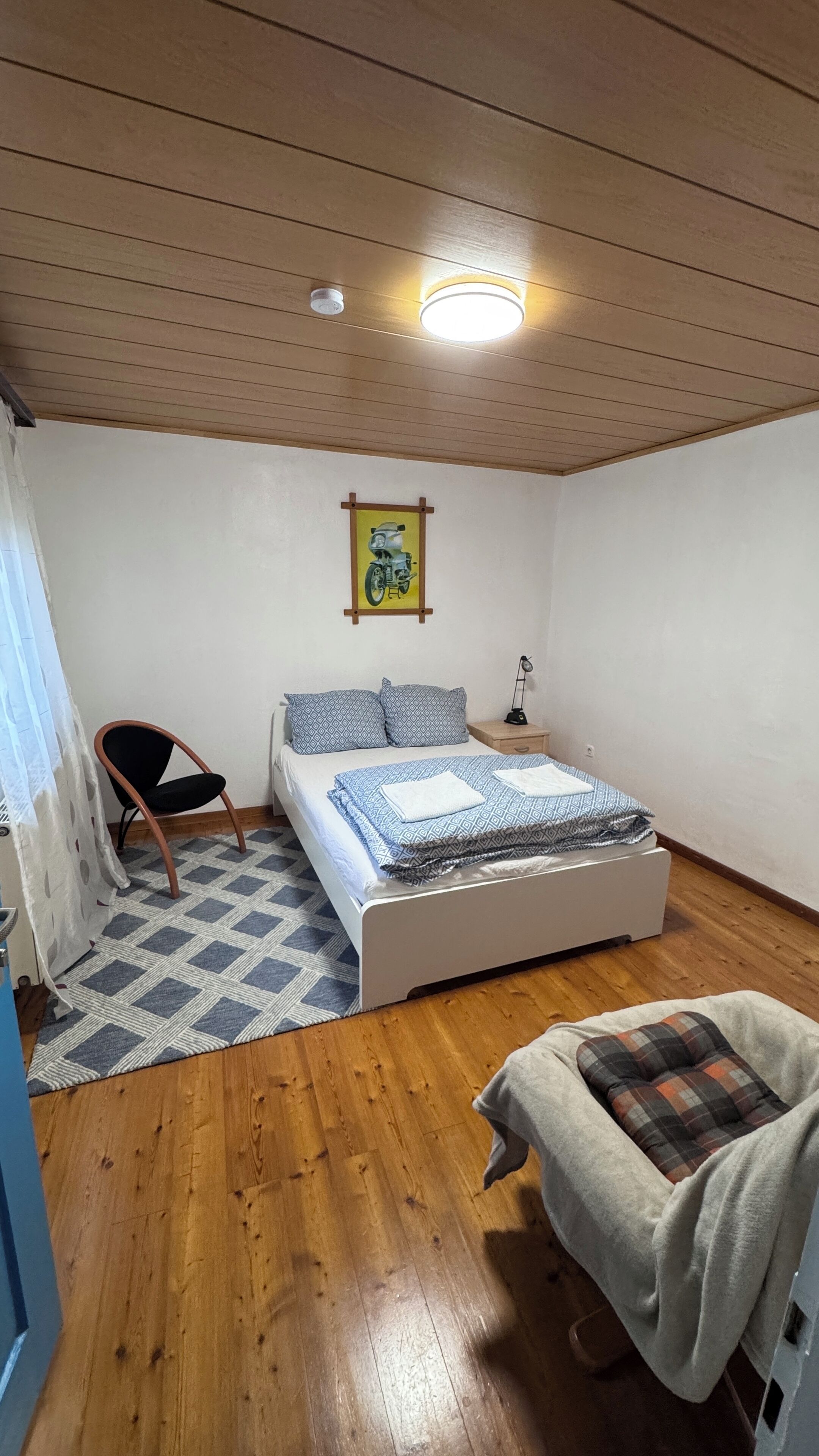 Ein Schlafzimmer mit Bett, Stuhl, Nachttisch, Lampe und einem Bild an der Wand.