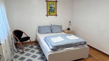 Ein Schlafzimmer mit Bett, Stuhl, Nachttisch, Lampe und einem Bild an der Wand.