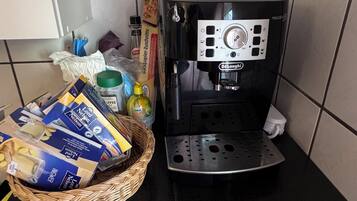Una cocina con cafetera, una cesta de pan y algunos alimentos envasados.