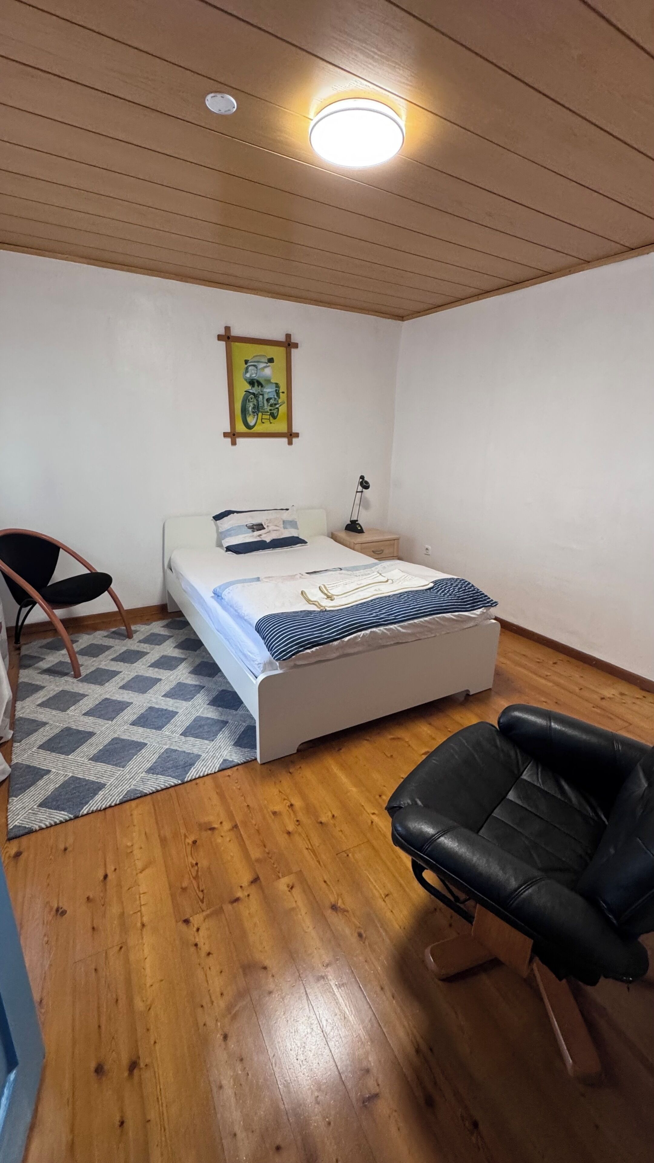A bedroom with a bed, a chair, a desk, a lamp, and a ceiling light.