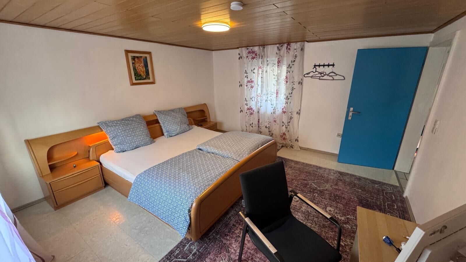 Et soveværelse med seng, natborde, stol, skrivebord, garderobe og dør.