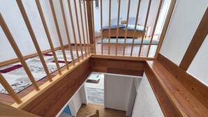 Een houten trap met een leuning, die leidt naar een kamer met een bed en een raam.