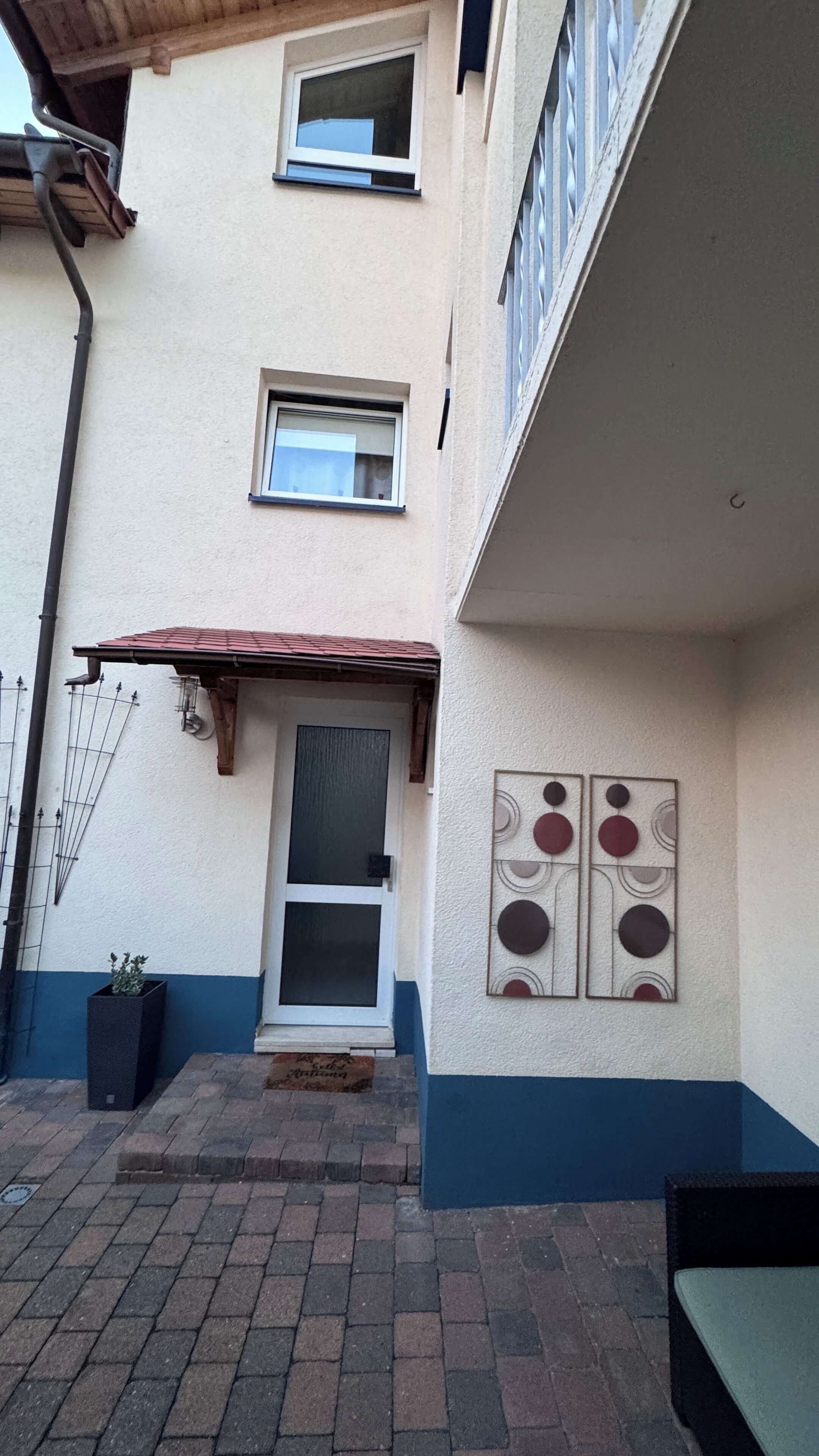 A two-story building with a small front porch, a window with a metal grill, and a wall-mounted artwork.