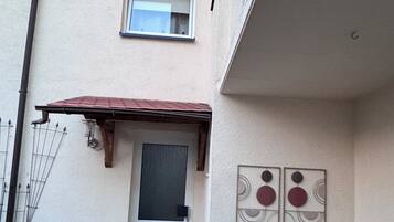A two-story building with a small front porch, a window with a metal grill, and a wall-mounted artwork.
