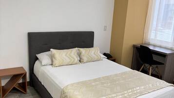 Un dormitorio ordenado con cama, escritorio y silla.