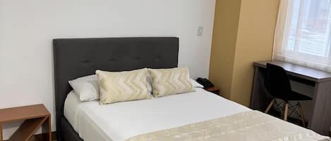 A neatly arranged bedroom with a bed, a desk, and a chair.