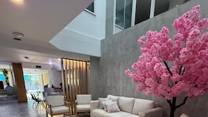 A modern interior with a sectional sofa, wooden chairs, and a decorative pink artificial tree. - Hotel Rosales Suites (Pereira)