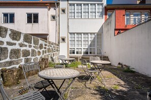 Um pátio com paredes de pedra, uma mesa e cadeiras de metal e um edifício com grandes janelas.