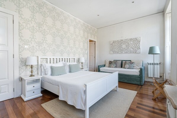 Quarto com cama grande, um sofá menor, mesa de cabeceira, abajur e radiador.
