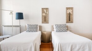 A hotel room with two beds, a radiator, a lamp, and two framed floral artworks on the wall. - GuestReady - House Marquês - Ponte S. João (Porto)