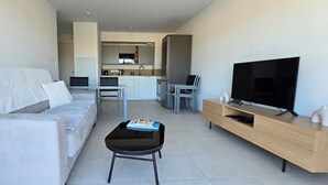 Ein modernes Wohnzimmer mit einer Couch, einem Couchtisch, einem Fernseher und einer Küchenzeile im Hintergrund.