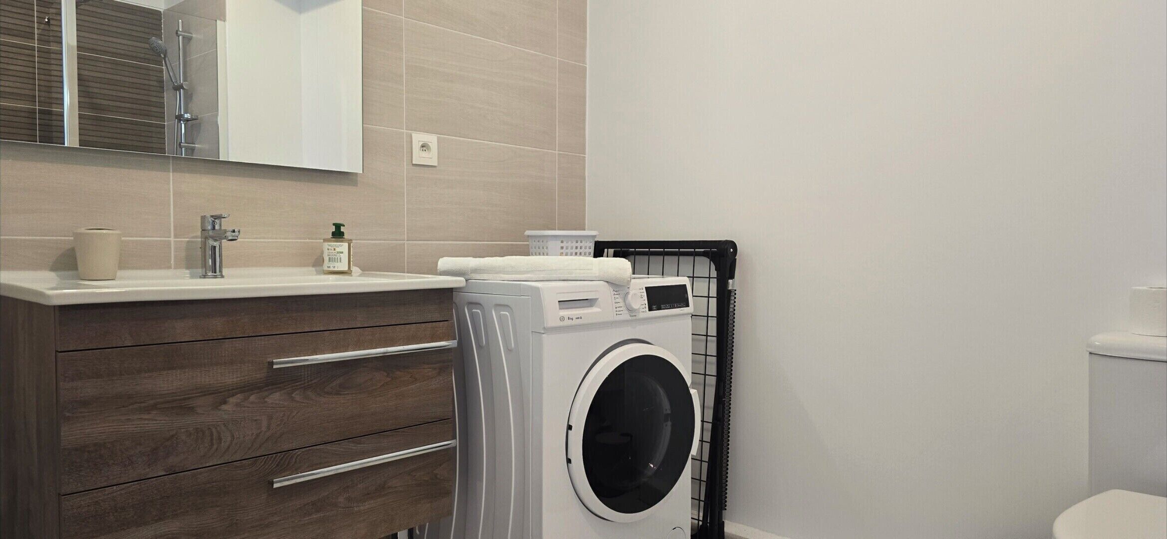 Une salle de bain moderne avec un meuble-lavabo en bois, un lave-linge et des toilettes.