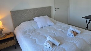 Ein ordentlich bezogenes Bett mit weißer Bettwäsche und Handtüchern, ein Nachttisch mit Lampe und ein kleiner Tisch neben dem Bett.