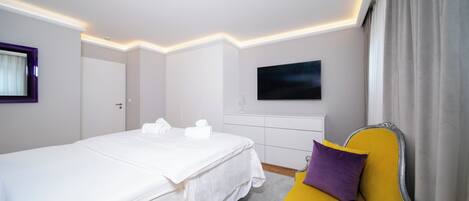 A hotel room with a bed, a yellow sofa, a flat-screen TV, and a window with curtains.