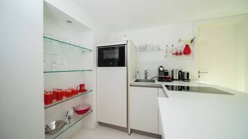A compact kitchen with white cabinets, a built-in oven, and glass shelves holding kitchenware.