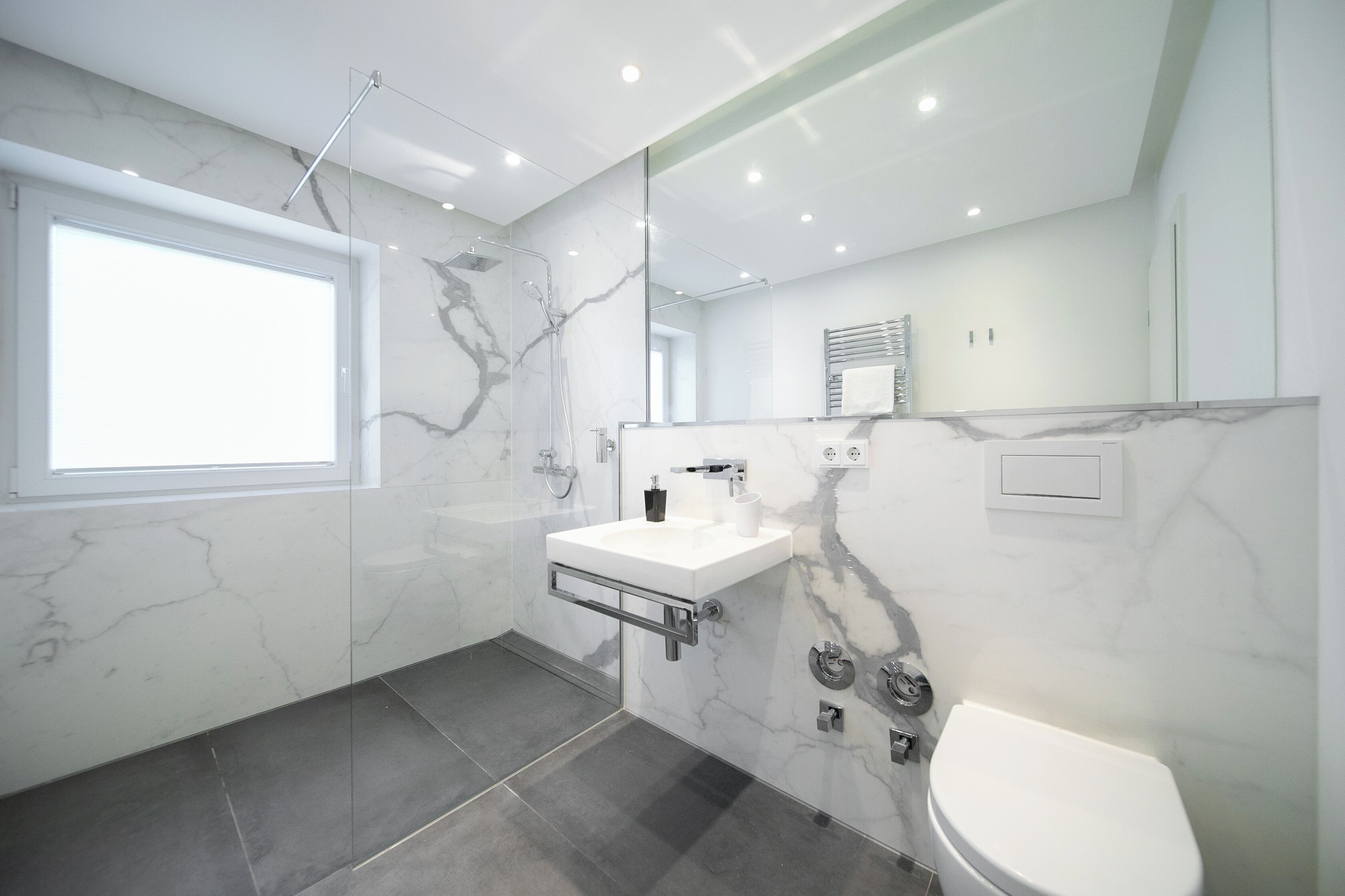Un baño moderno con cabina de ducha de vidrio, un lavabo blanco con encimera de mármol y un inodoro.