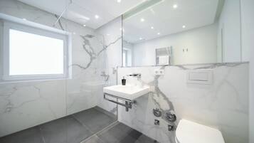 Un baño moderno con cabina de ducha de vidrio, un lavabo blanco con encimera de mármol y un inodoro.
