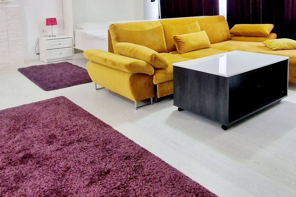 A modern living room with a yellow sofa, a black coffee table, and purple rugs.