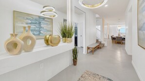 Un pasillo moderno con pared blanca, un cuadro y jarrones decorativos. Se ve una escalera que conduce a otra habitación.