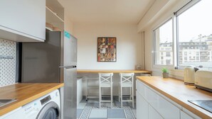 Une cuisine compacte équipée d’un lave-linge, d’un réfrigérateur et d’une fenêtre donnant sur la ville.