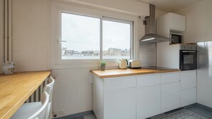 Une cuisine moderne avec des armoires blanches, un comptoir en bois, un four à micro-ondes encastré, une hotte de cuisinière en acier inoxydable et une fenêtre donnant sur la ville.