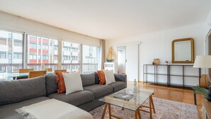 Un salon moderne avec un canapé gris, une table basse en verre et un tapis à motifs.