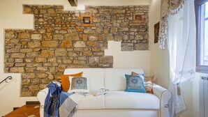 A cozy room with a white sofa, a stone wall, and a window with curtains. - Oriuolo - Flo Apartments (Firenze)