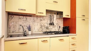 A kitchen with marble backsplash, yellow cabinets, and stainless steel appliances. - JOIVY Welcoming flat in Porta Garibaldi (Milan)